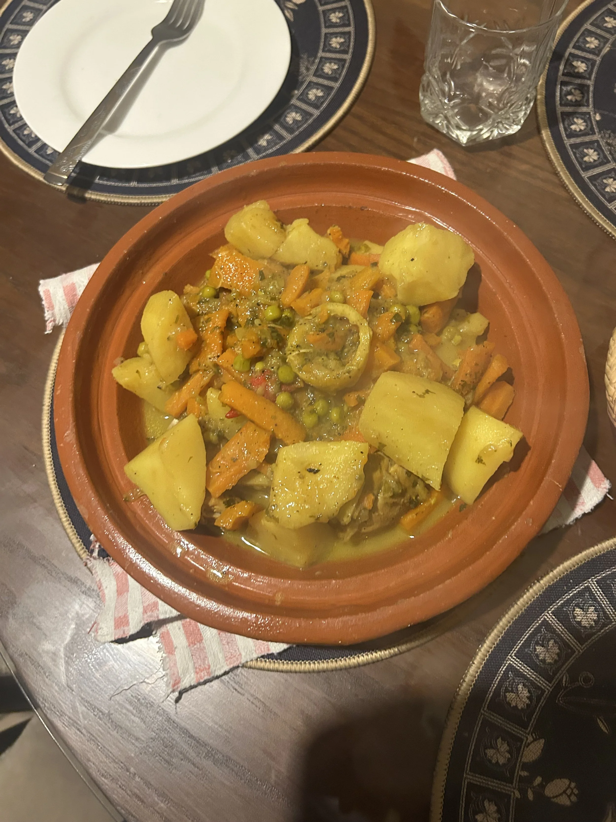 A chicken tagine with peas, carrots, and potatoes sits on a table