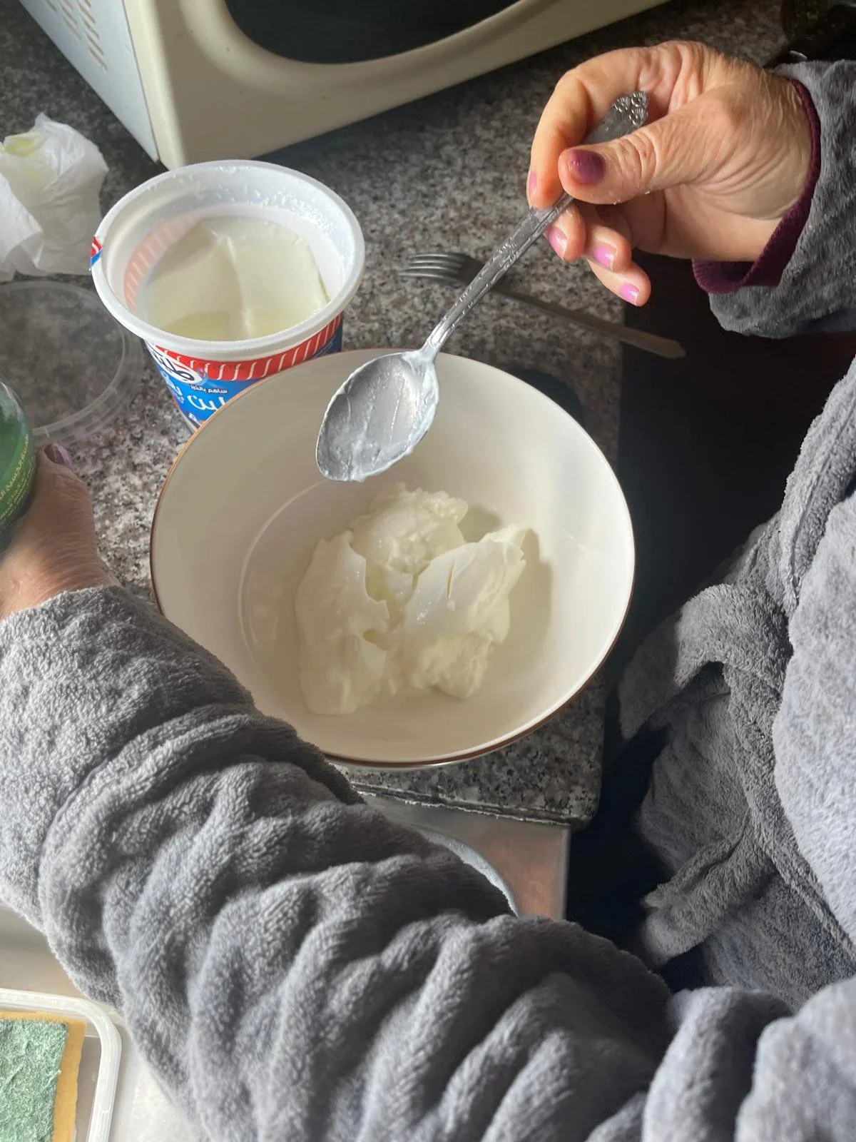 Someone spoons leben from a plastic container into a bowl.