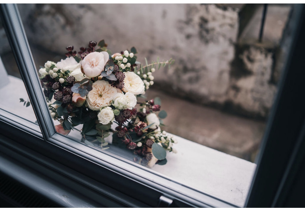 White and dark purple brides bouquet with peonies, eucalyptus, peach roses and astrantia sitting on a window sill for a spring bride.