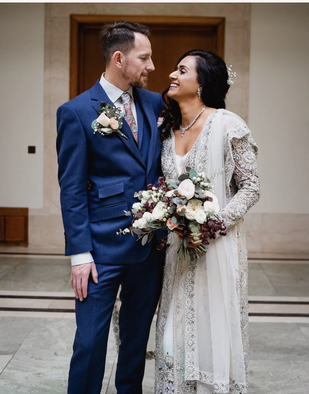 The happy couple with their white and dark purple brides bouquet with peonies, eucalyptus, peach roses and astrantia and his button hole to match the bouquet in Hackney town Hall.