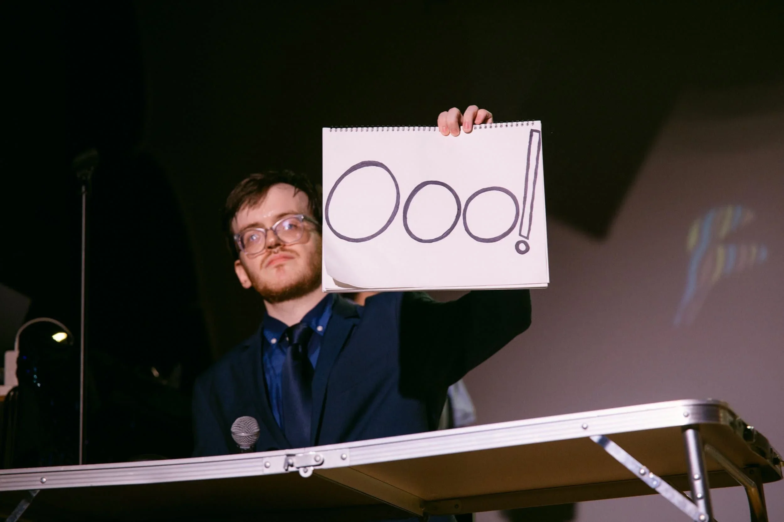 Comedian On Stage Holding a Notepad FAD 2024.webp