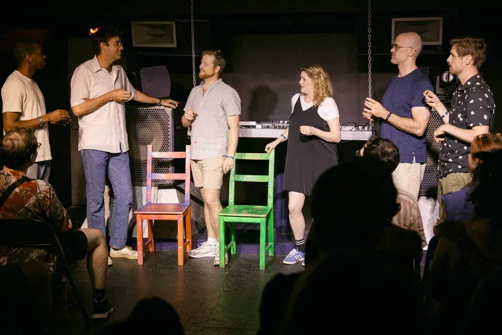 Photo of Eris Deepspace featuring performers in a dark room with colorful chairs