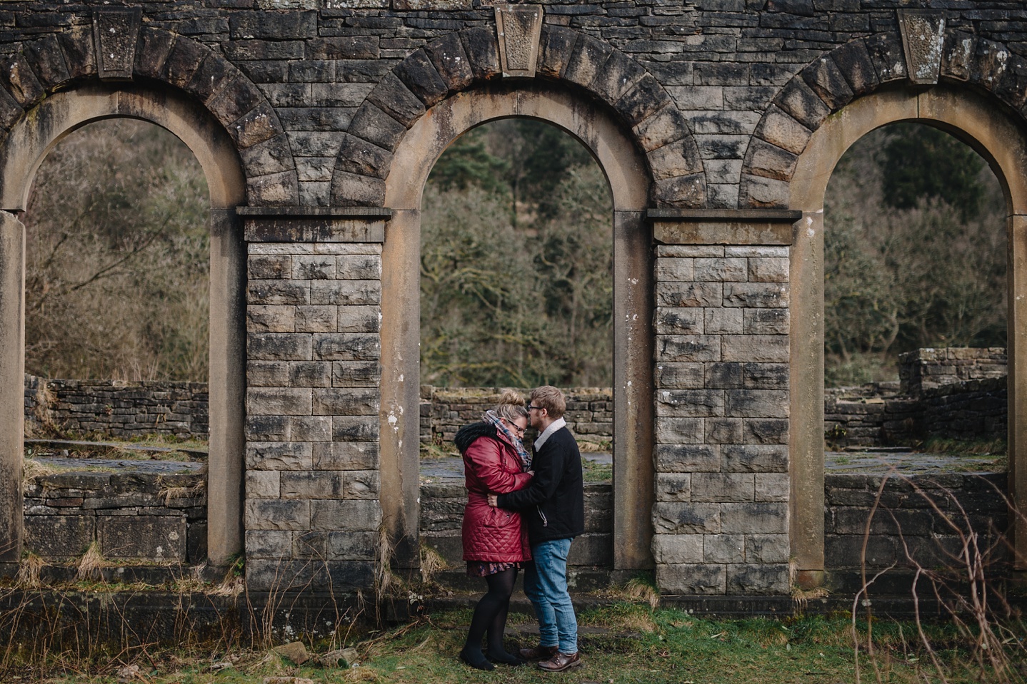 engagement shoot of man and woman cuddling stood infront of the ruin of Errwood Hall
