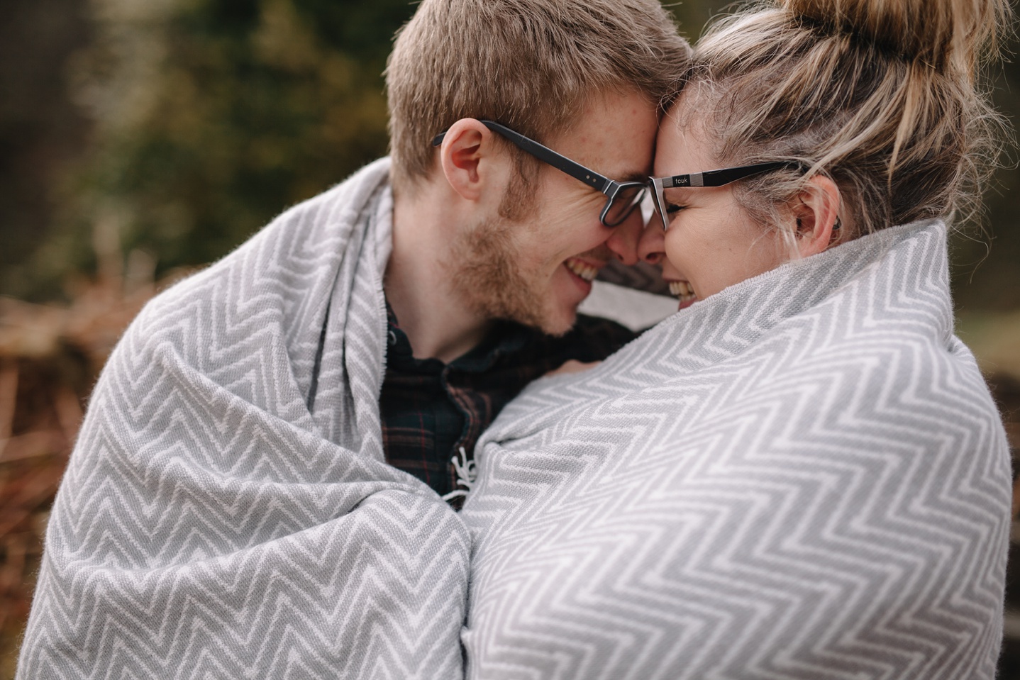 engagement photography of man and woman wrapped up in a grey blanket cuddling