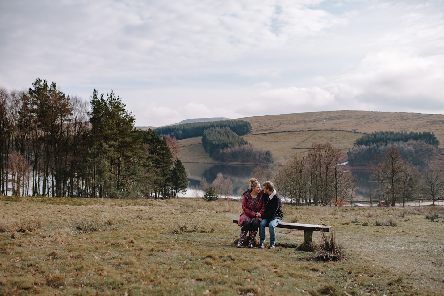 Engagement shoot of man and woman sat on a bench with views of the Goyt Valley