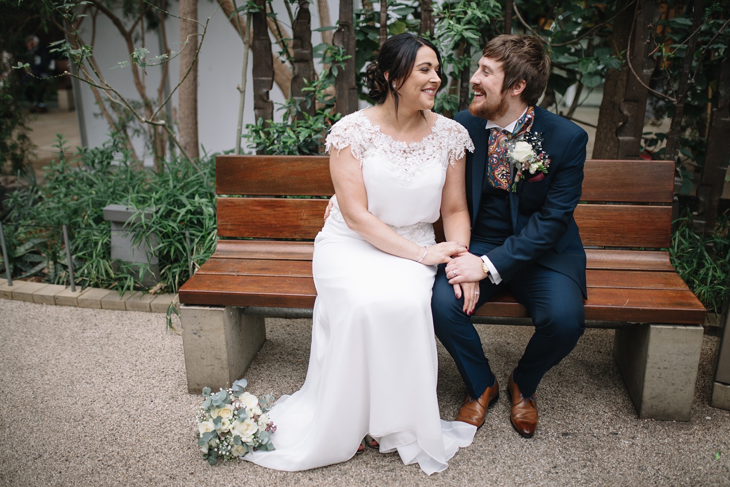 bride and groom sat on a bench smiling in the Sheffield Winter Gardens
