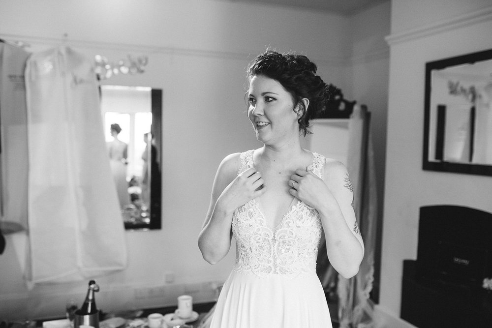 black and white image of bride smiling whilst getting ready into her wedding dress at Whirlowbrook Hall