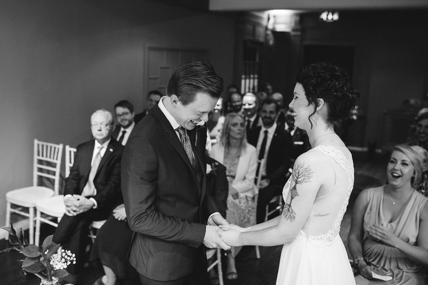 black and white photo of groom laughing whilst saying his vows
