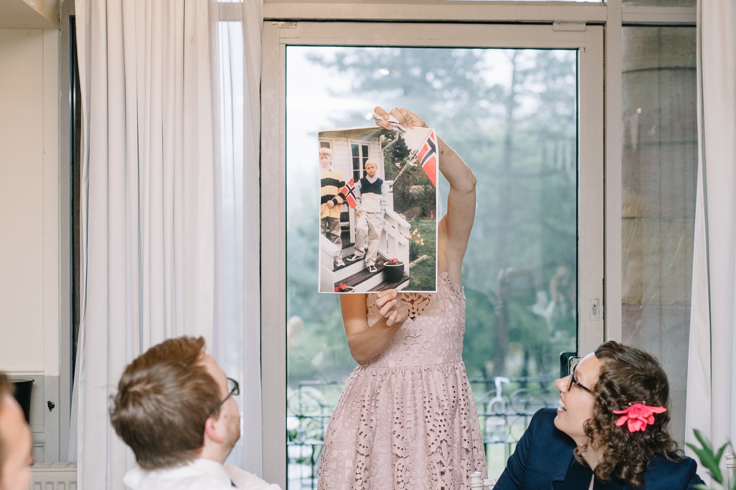 grooms sister holding up embarrassing childhood photo of groom 