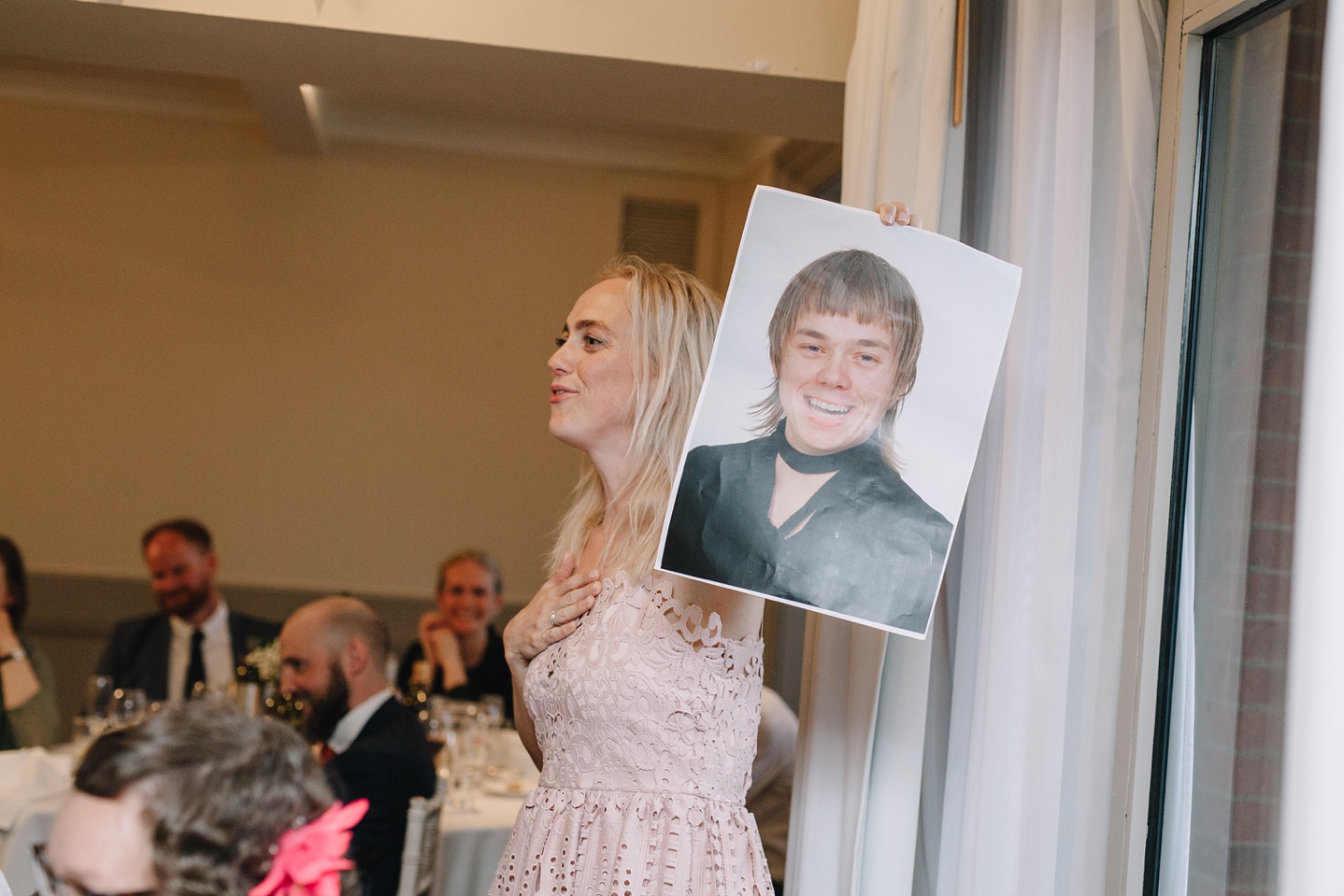 grooms sister holding up embarrassing photo of groom