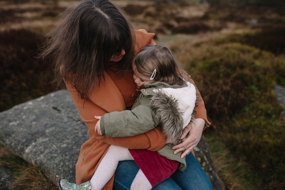 mum and little girl sat on a rock having a big cuddle