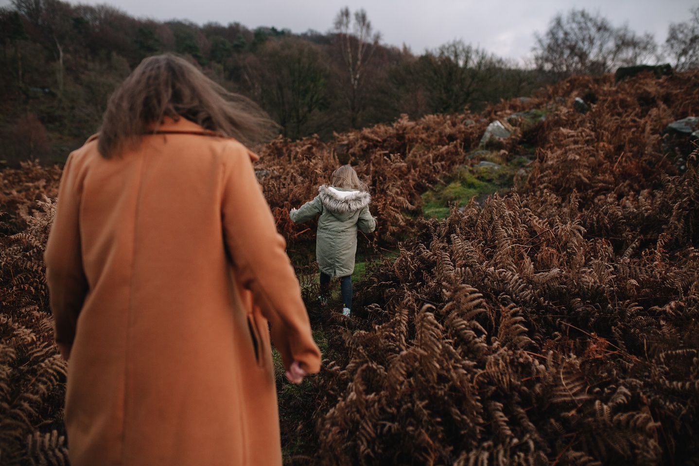 mum and little girl walking through the brown ferns
