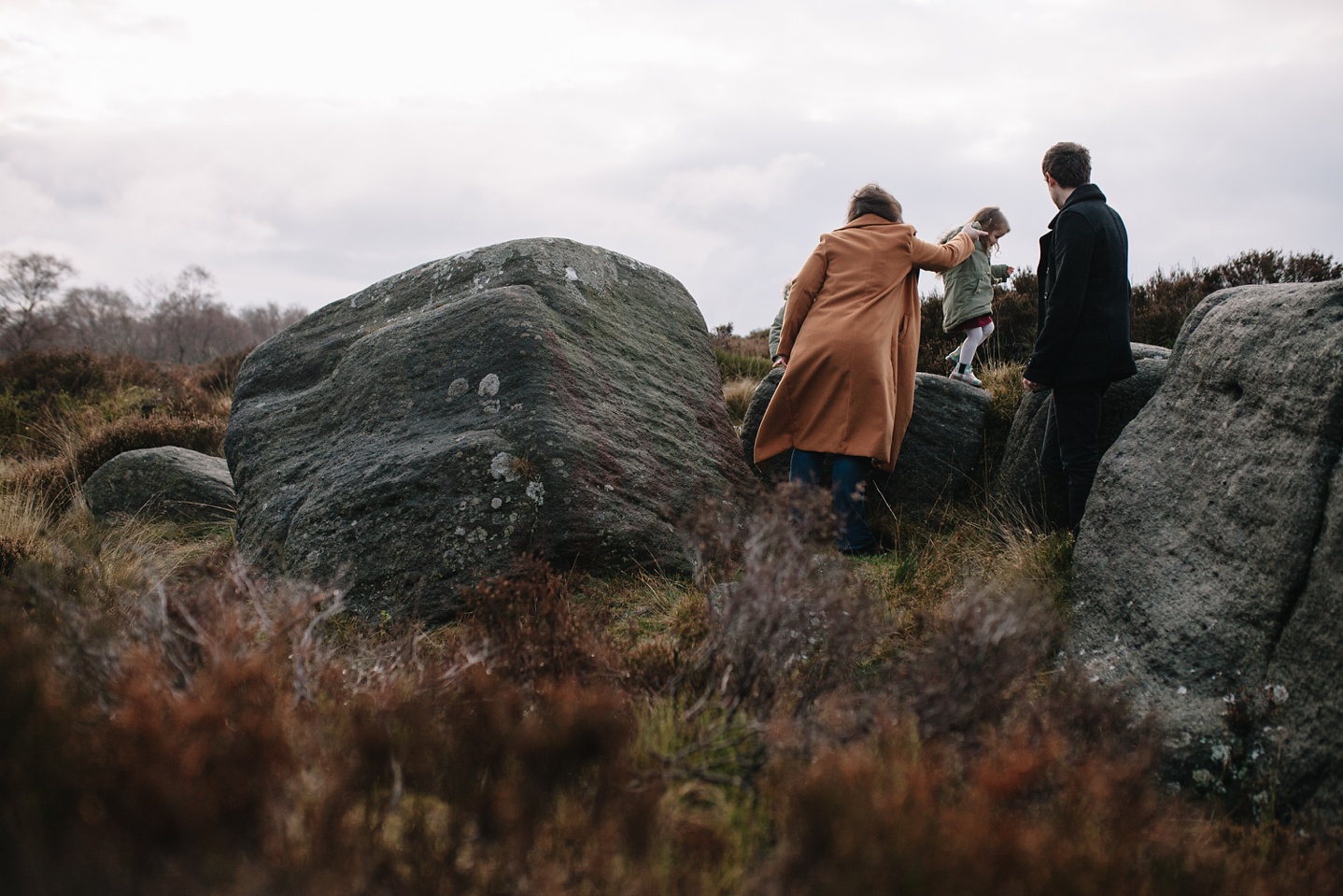 Mum and dad helping little girl to climb a rock