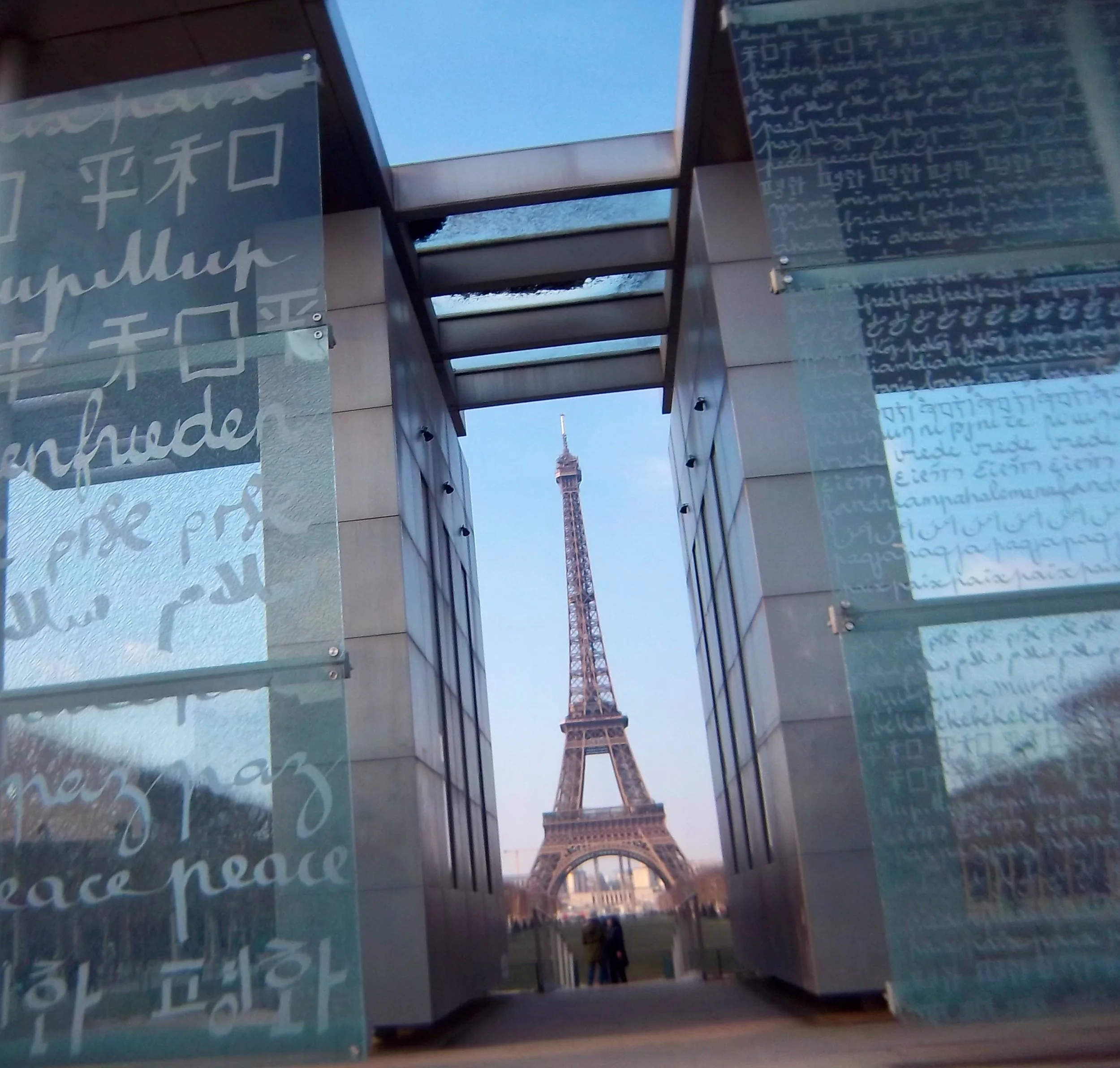 Eiffel Tower in Paris seen next to glass walls of the word Peace in every language