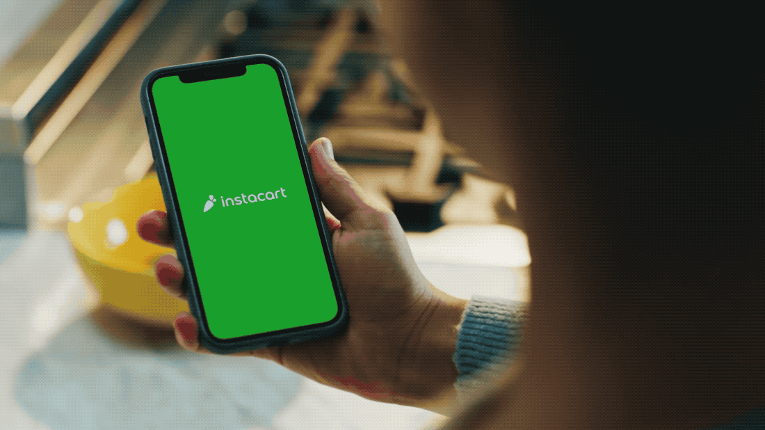 Person holding a smartphone displaying the Instacart app logo in green screen