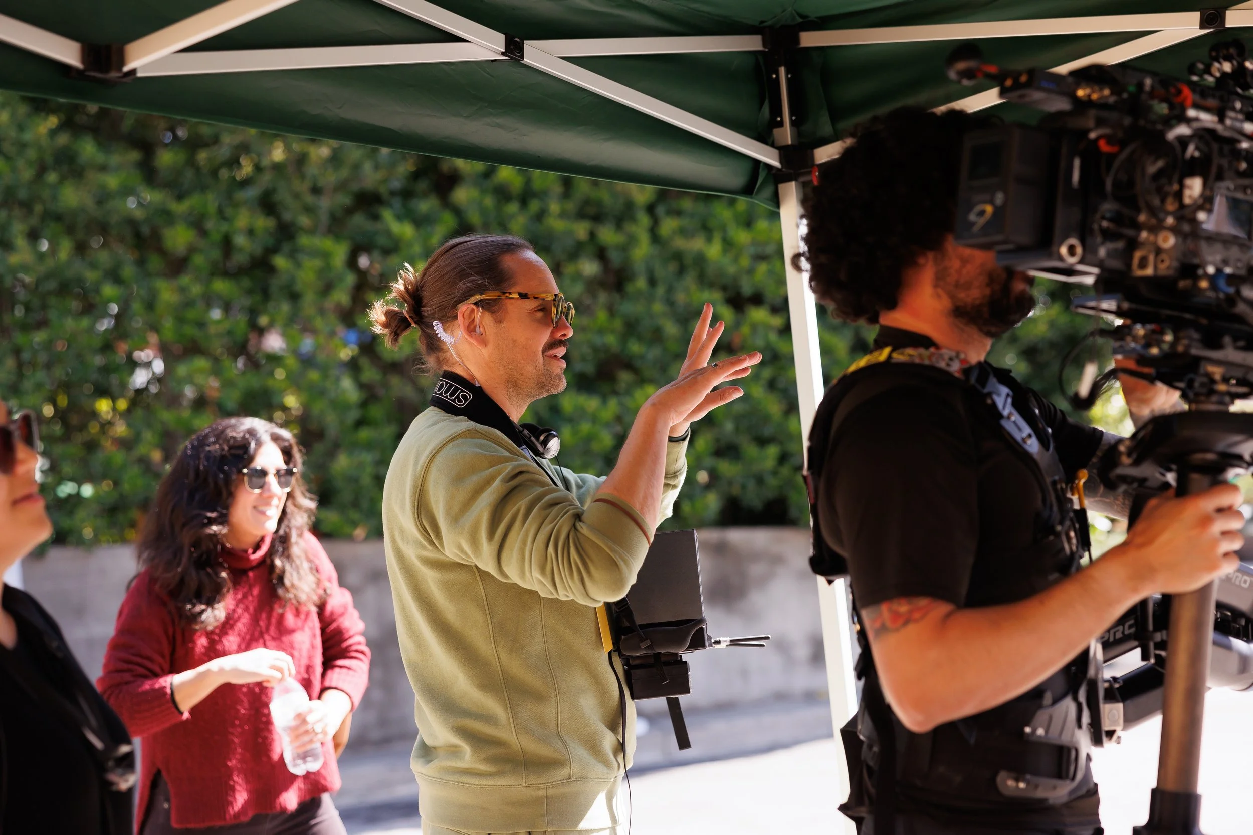 Film director giving instructions on set with camera operator and team under green canopy outside