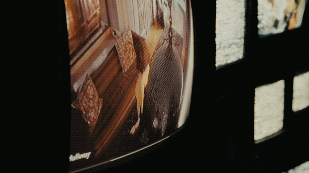 A television screen showing a person with a dark hat and coat, reflected on the screen, with window light reflections on the right side of the image.