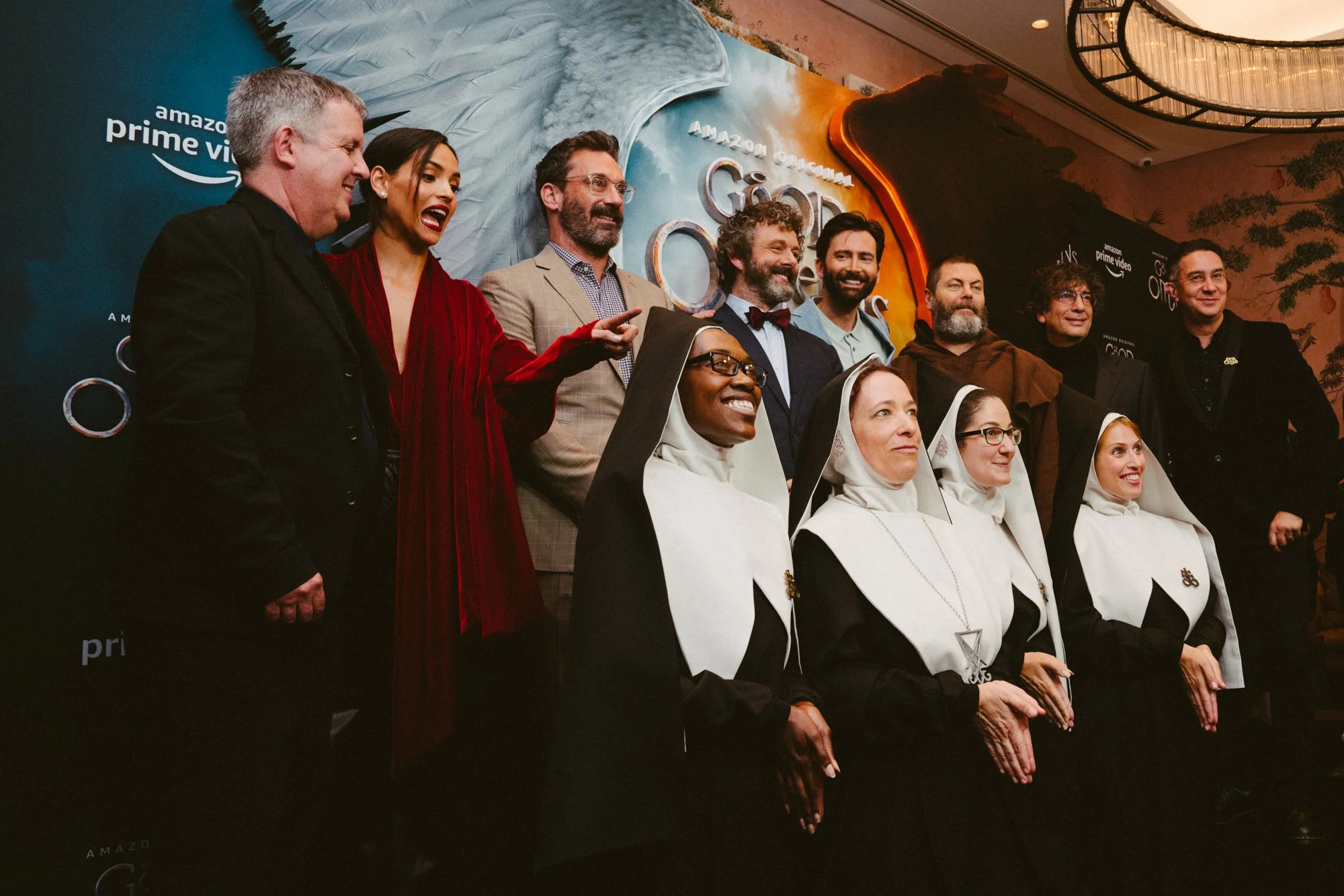 Group photo of people, including nuns and filmmakers, at a promotional event for Amazon Prime Video's 'Gilded Age' in front of a backdrop featuring a bird and mountains.