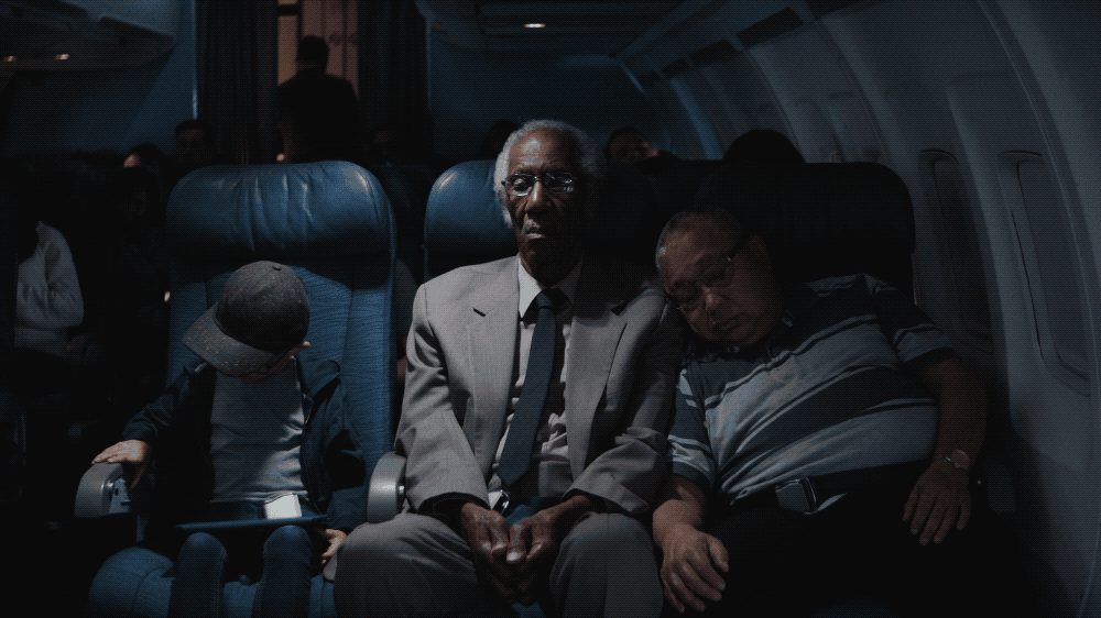 Passengers seated on an airplane, including a young child with a cap and identity card, an elderly man in a suit, and a middle-aged man resting on the window seat, all appearing tired or asleep.