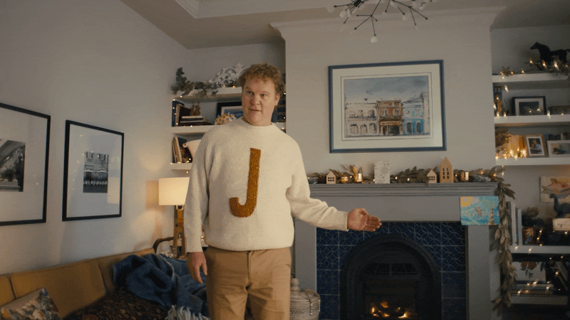 A person standing in a living room holding a large letter J.