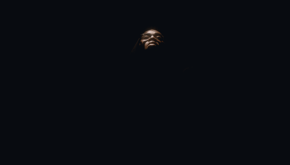 Close-up of a person illuminated by light and partially hidden in darkness, with the face visible against a dark background.