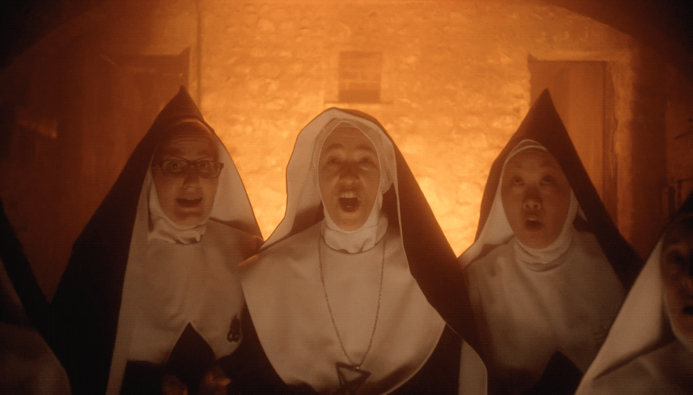 People dressed as nuns with hoods on, making surprised or shouting expressions, illuminated by warm orange light.