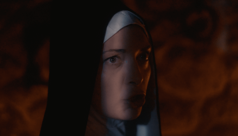 A woman dressed as a nun with a veil, looking intensely at the camera in a dark, smoky atmosphere.