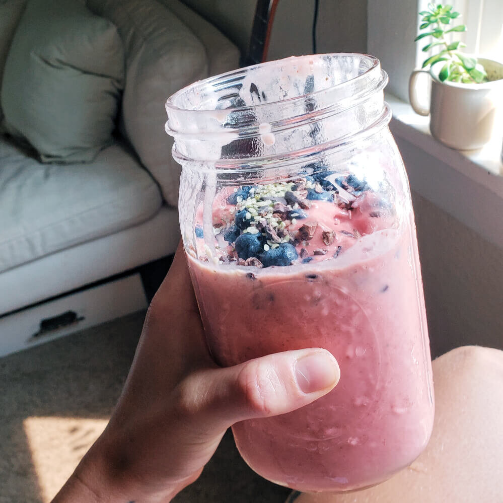 strawberry smoothie with cacao nibs in a mason jar topped with hemp seeds and blueberries