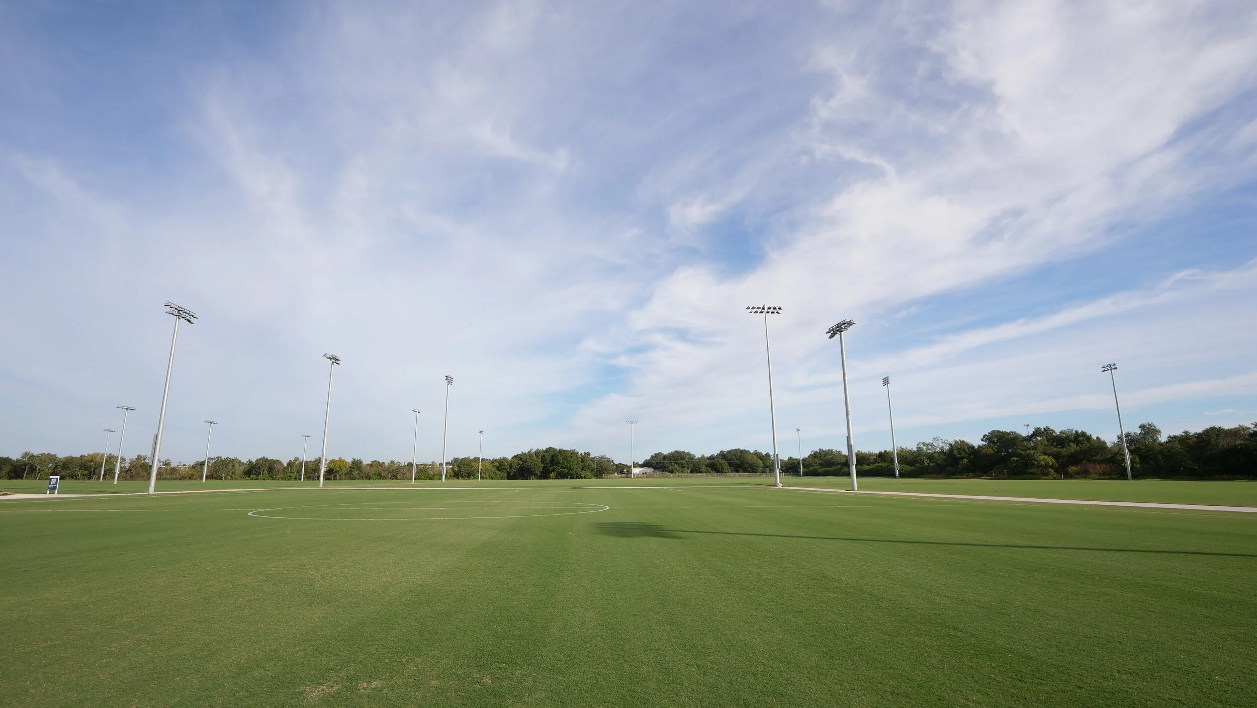 Stratus clouds are seen over a field with stadium light from middle of a field. 