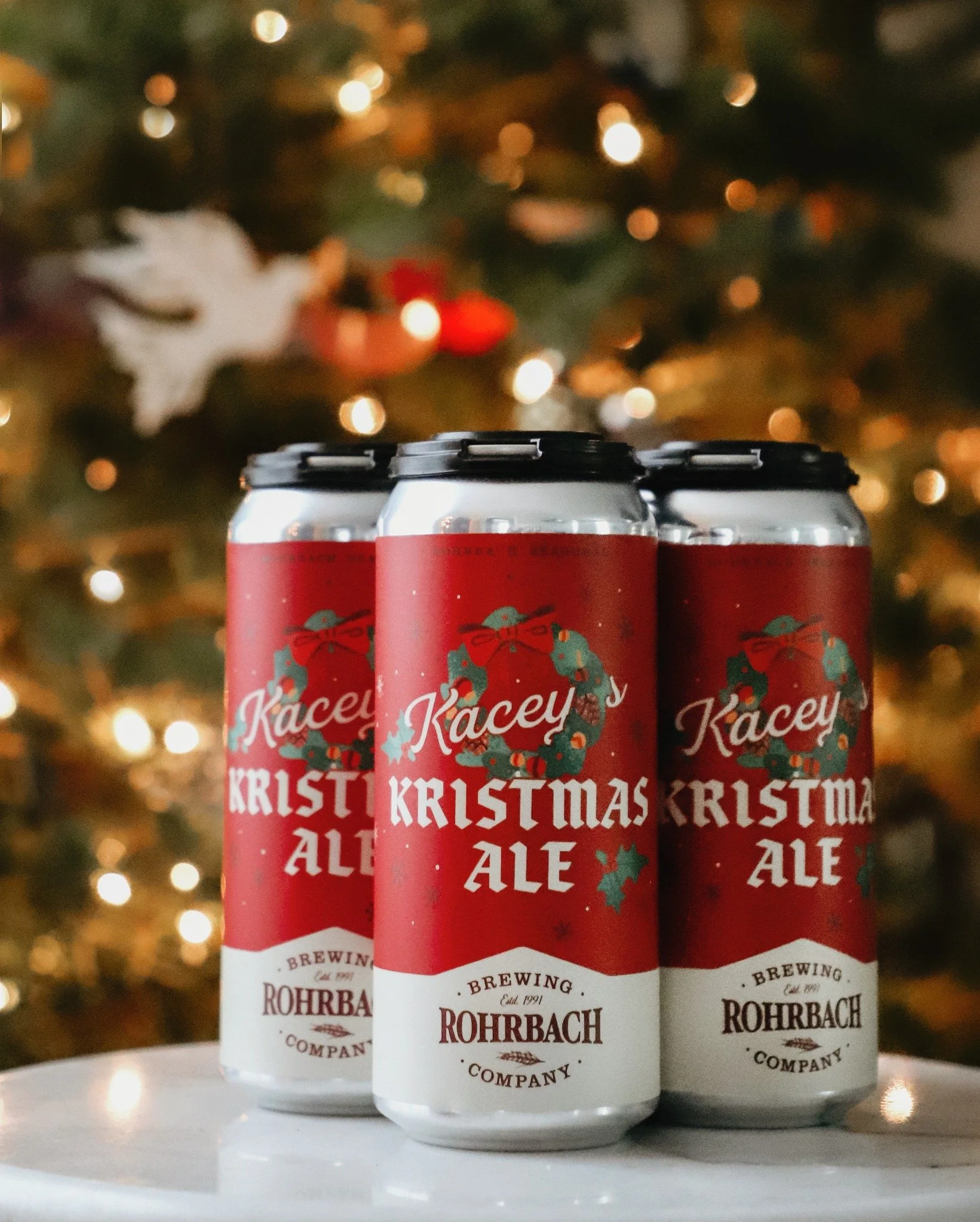 4-pack of red Rohrbach Kacey's Kristmas Ale with a blurry christmas tree in the background