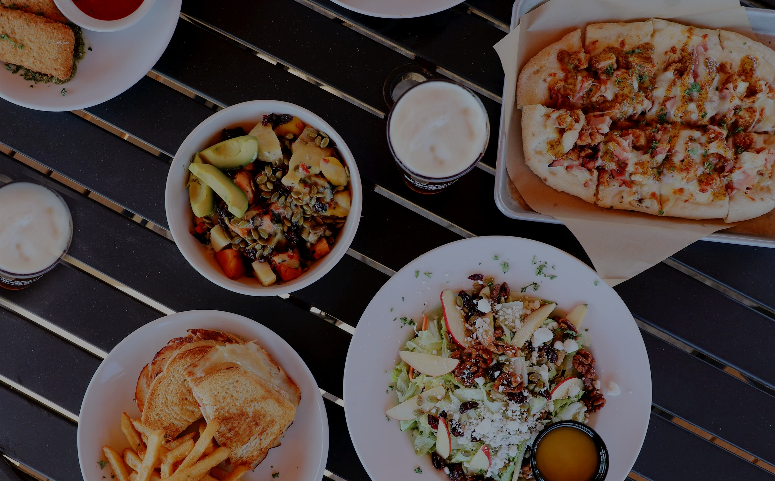 Overhead view of Rohrbach beers with flatbread, salad, sandwiches, fries, and a grain bowl.