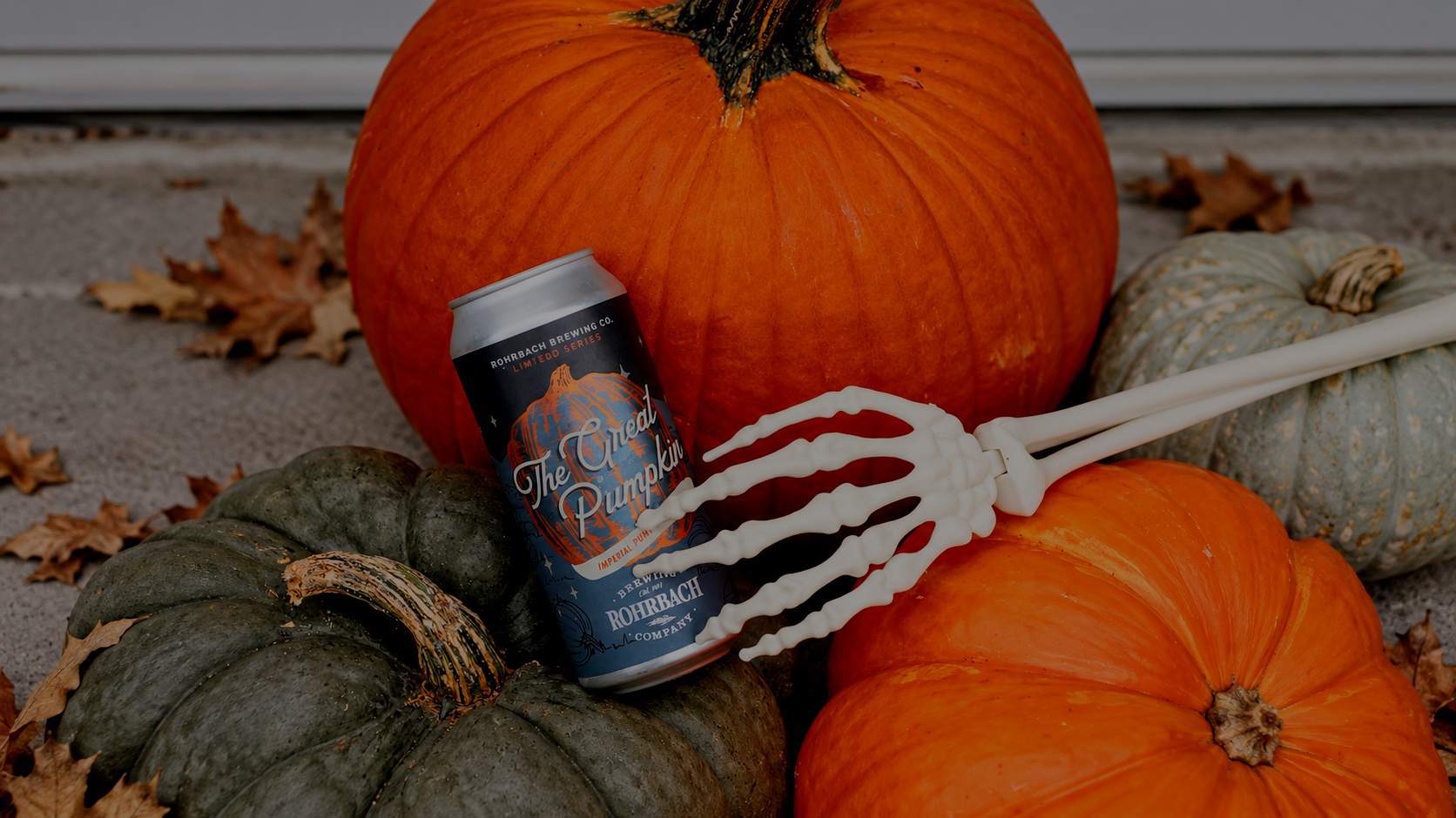 Rohrbach The Great Pumpkin Imperial Pumpkin Ale can held by a skeleton hand among autumn pumpkins.