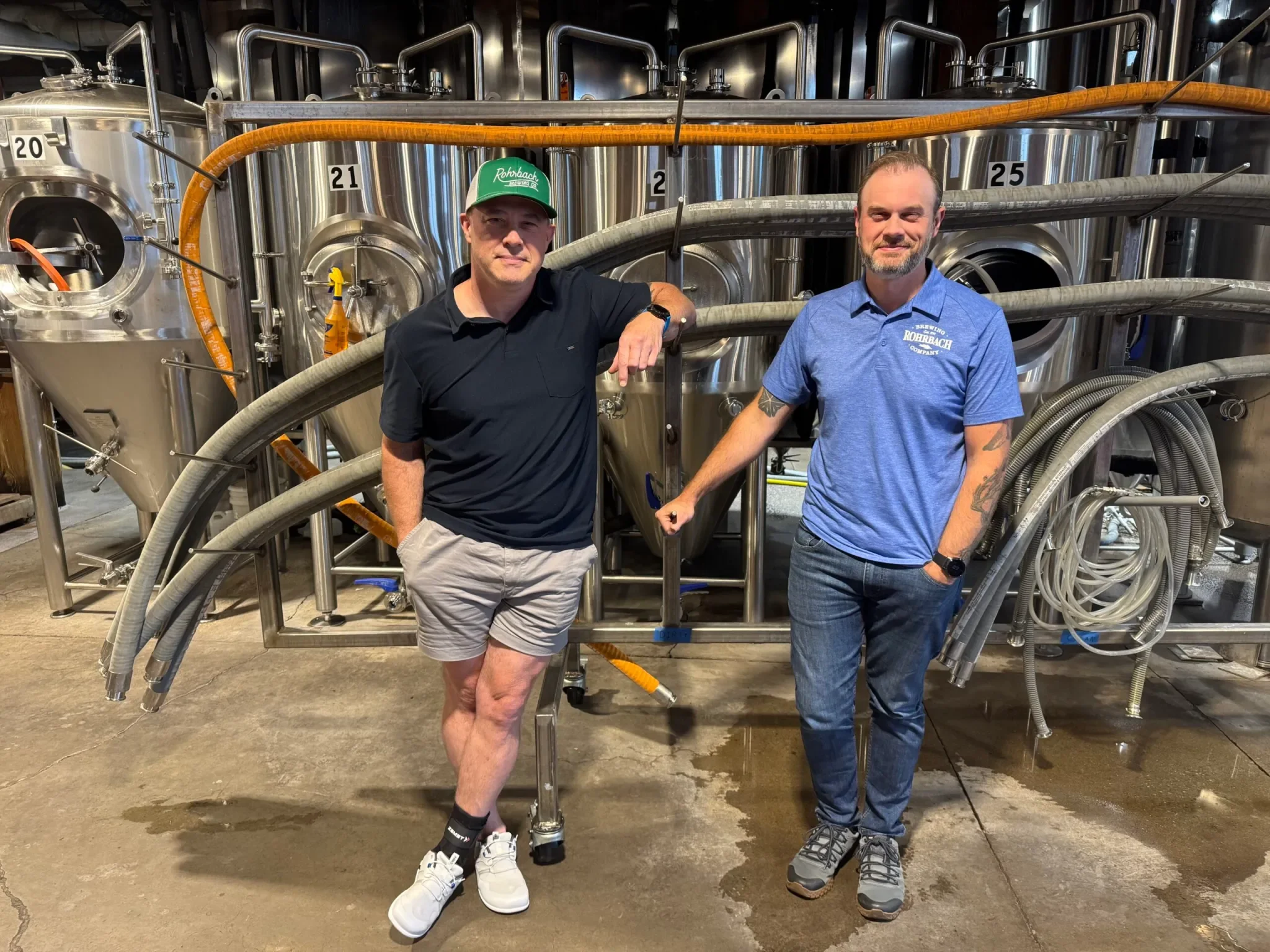 Rohrbach owners standing inside the brewery in front of stainless steel brewing tanks.