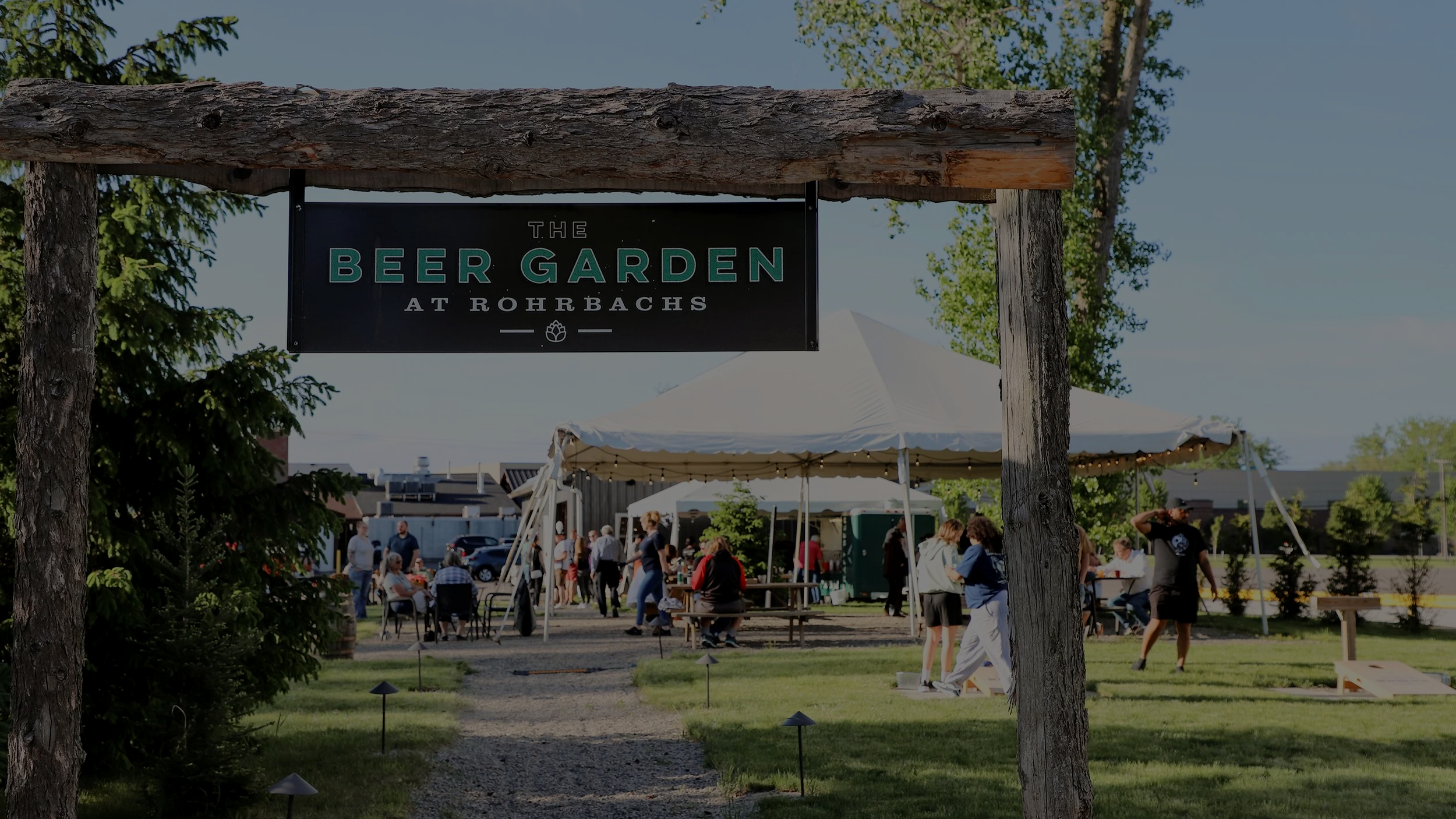 Beer Garden entrance at Rohrbach Brewing Co. with a wooden sign, outdoor tent, lawn games, and guests enjoying a sunny afternoon.