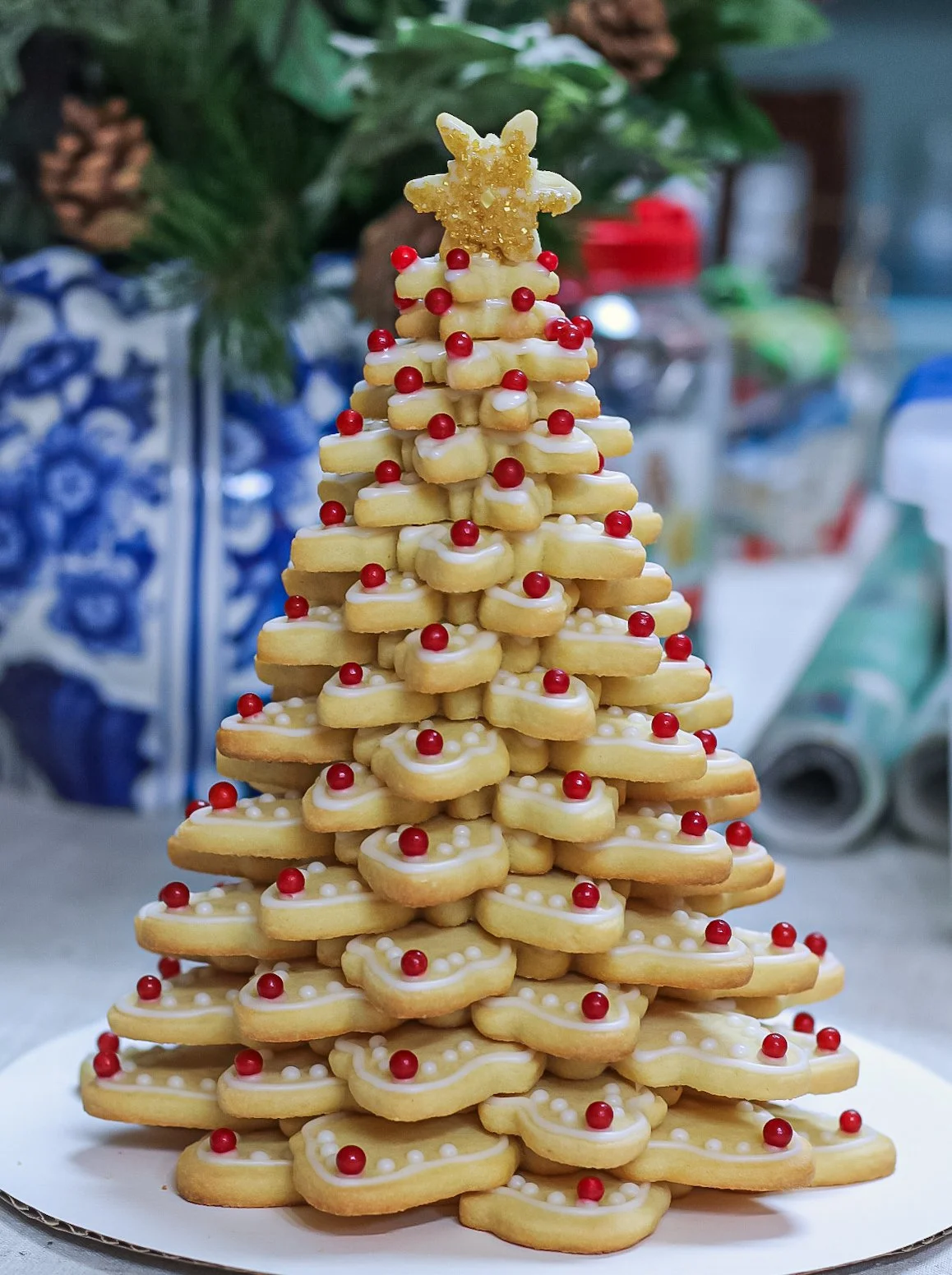 A Christmas tree made of stacked sugar cookies decorated with white icing, red sugar pearls, and a star-shaped cookie at the top.