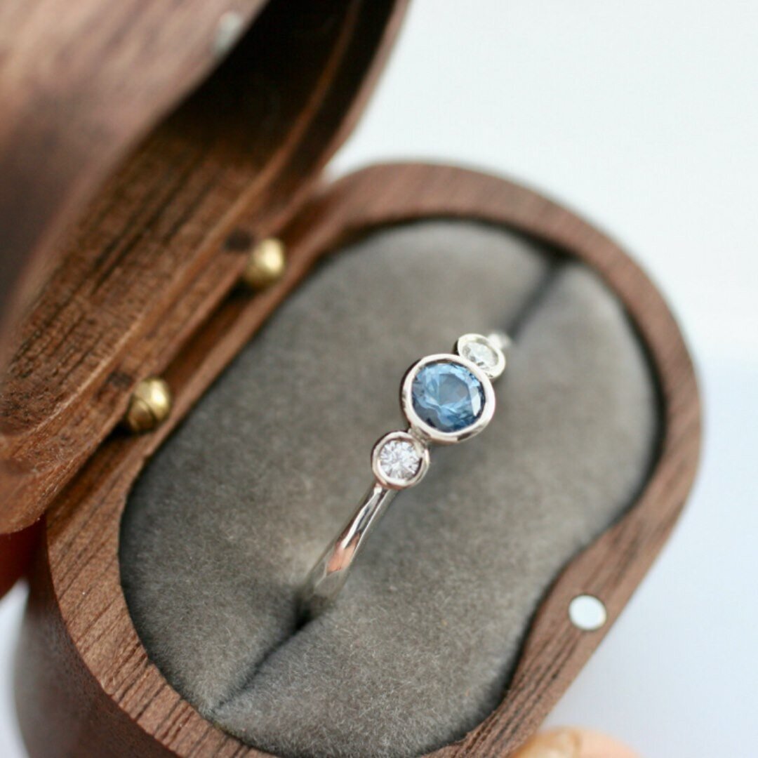 Clear and extremely pretty ethically sourced 4mm Malawi mid blue sapphire, set in a tapered recycled 14ct yellow gold bezel setting. 

This ring also has two sweet 2mm recycled white diamonds set either side, on a hammered tapered silver band. 

This