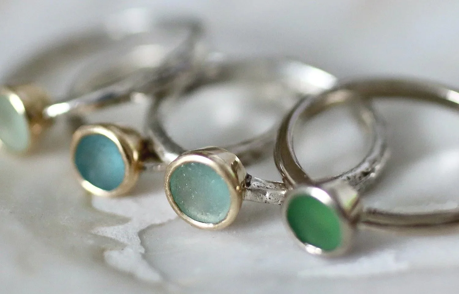 Group of Glasswing Jewellery handmade sea glass rings on a shell in different shades of green