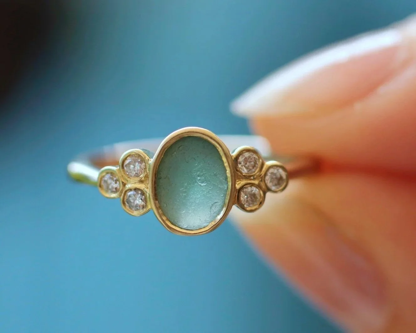 Godreva sea glass engagement ring with green sea glass held up to the light between two fingers