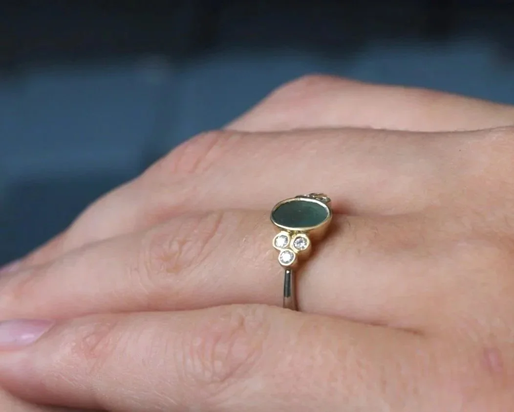 Green sea glass, diamond and gold engagement ring worn on a hand