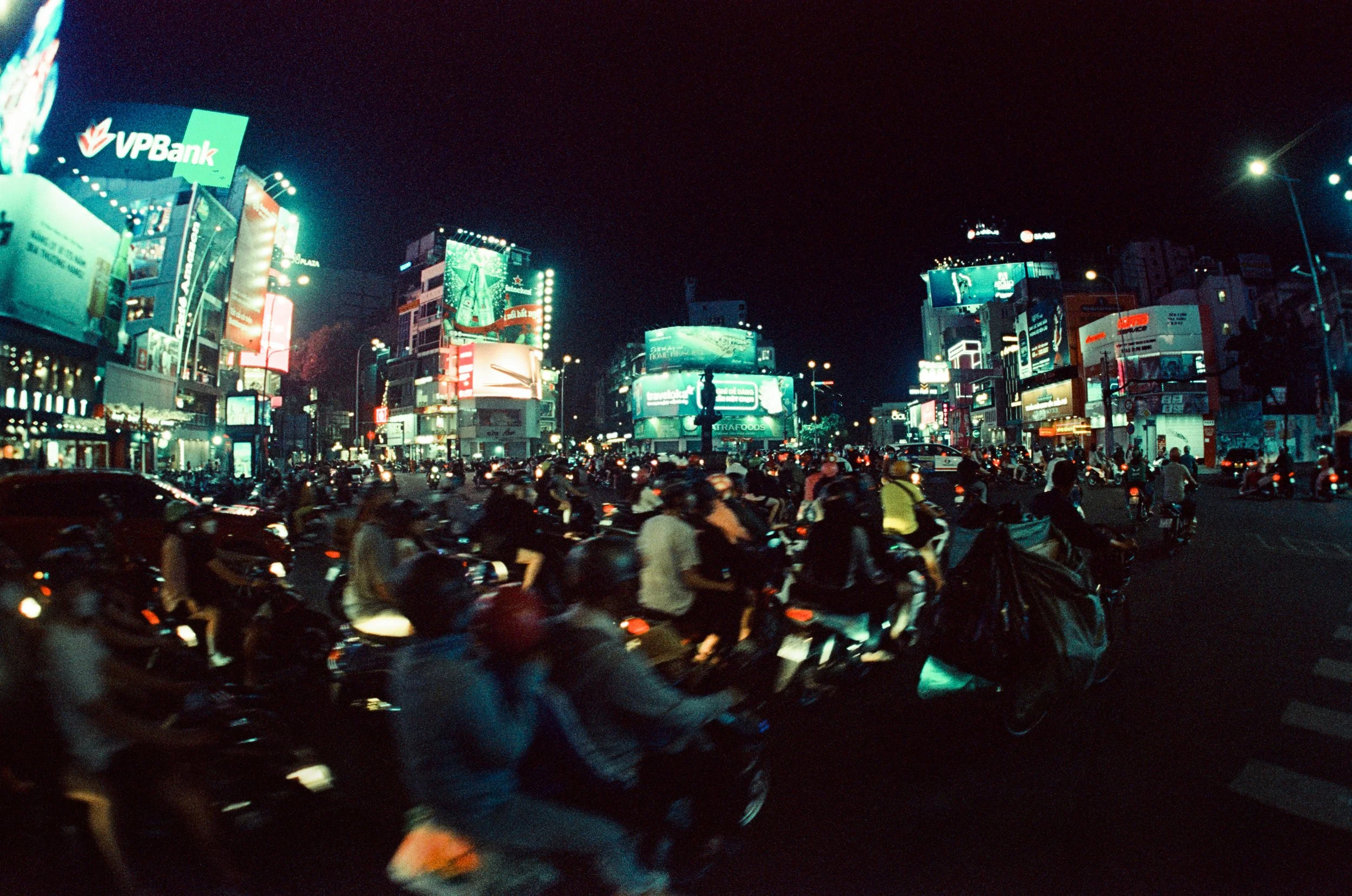 Blured figures riding across a wide open space in low light cityscape