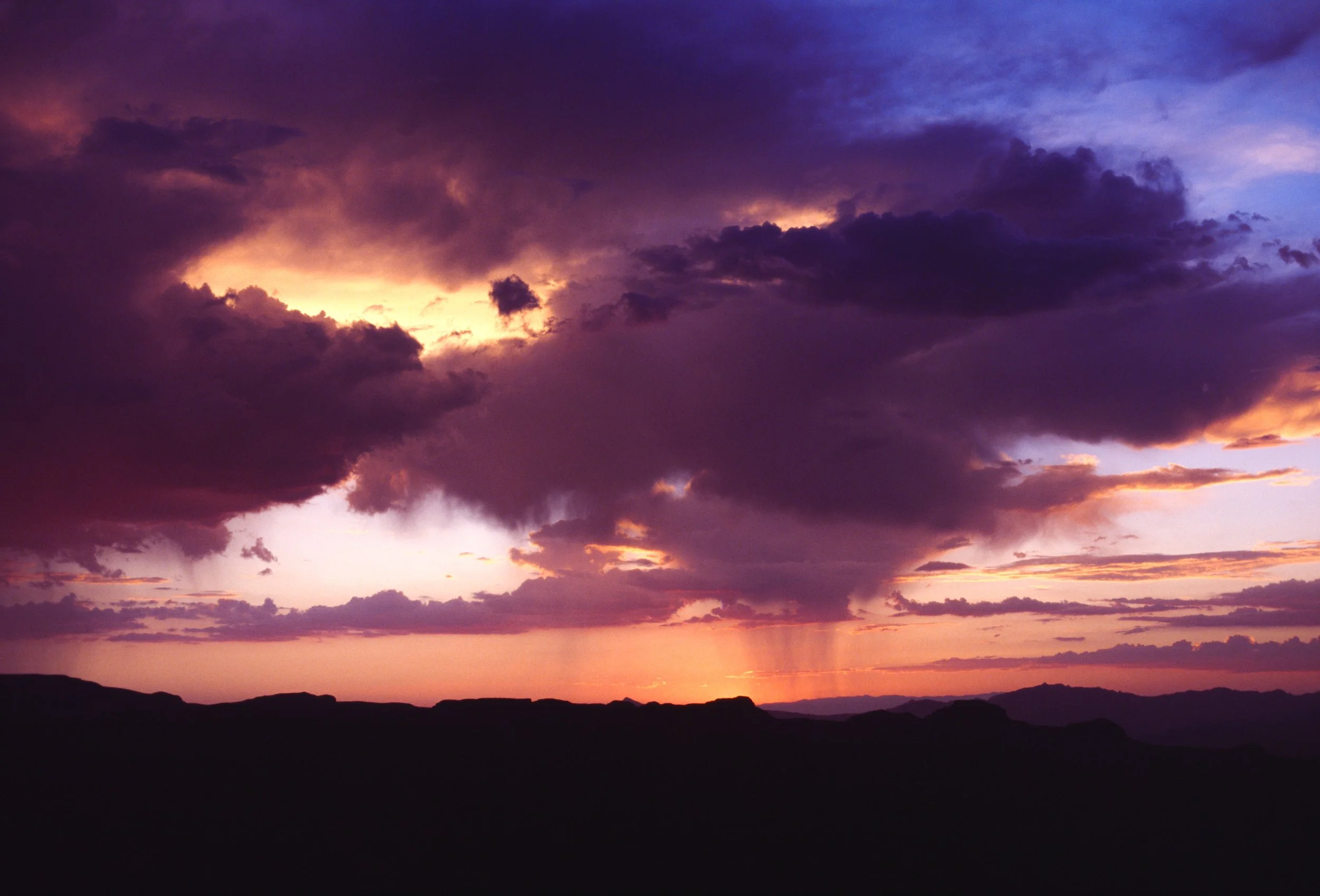 Storm clouds and rain shafts illuminated by sunset over the Grand Canyon