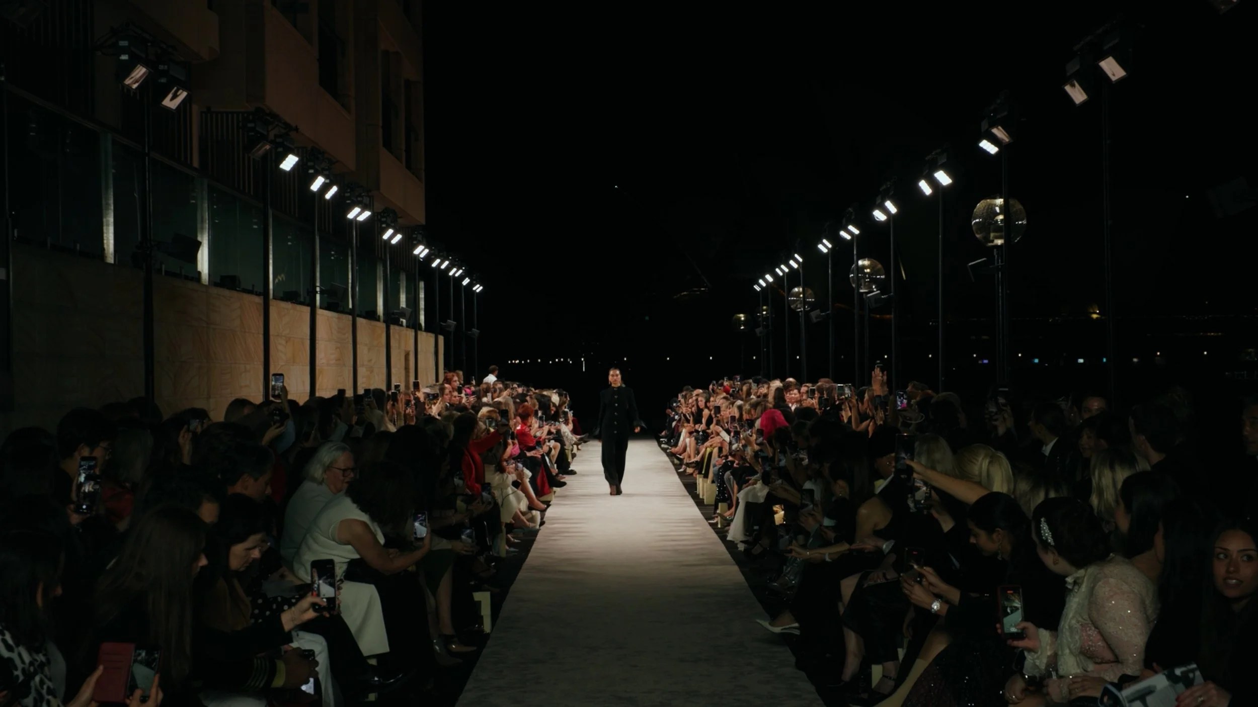 Wide angle low light runway cinematography at Australian Fashion Week nighttime outdoor show.