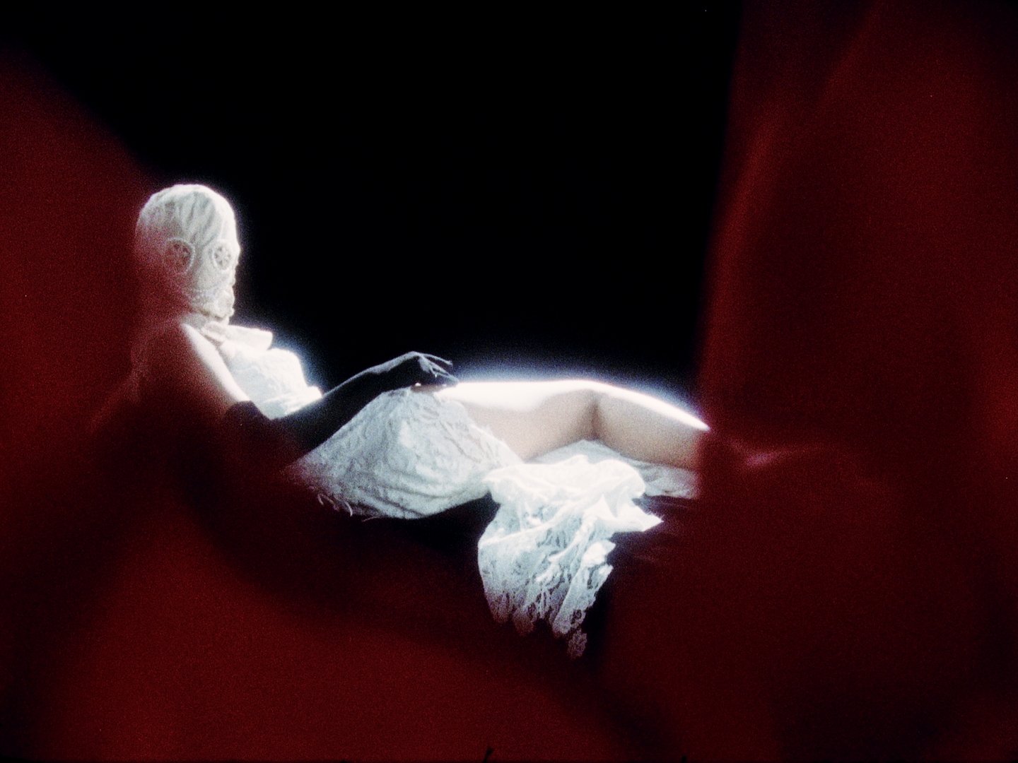 A woman reclining on a lounge beneath red curtains in low light