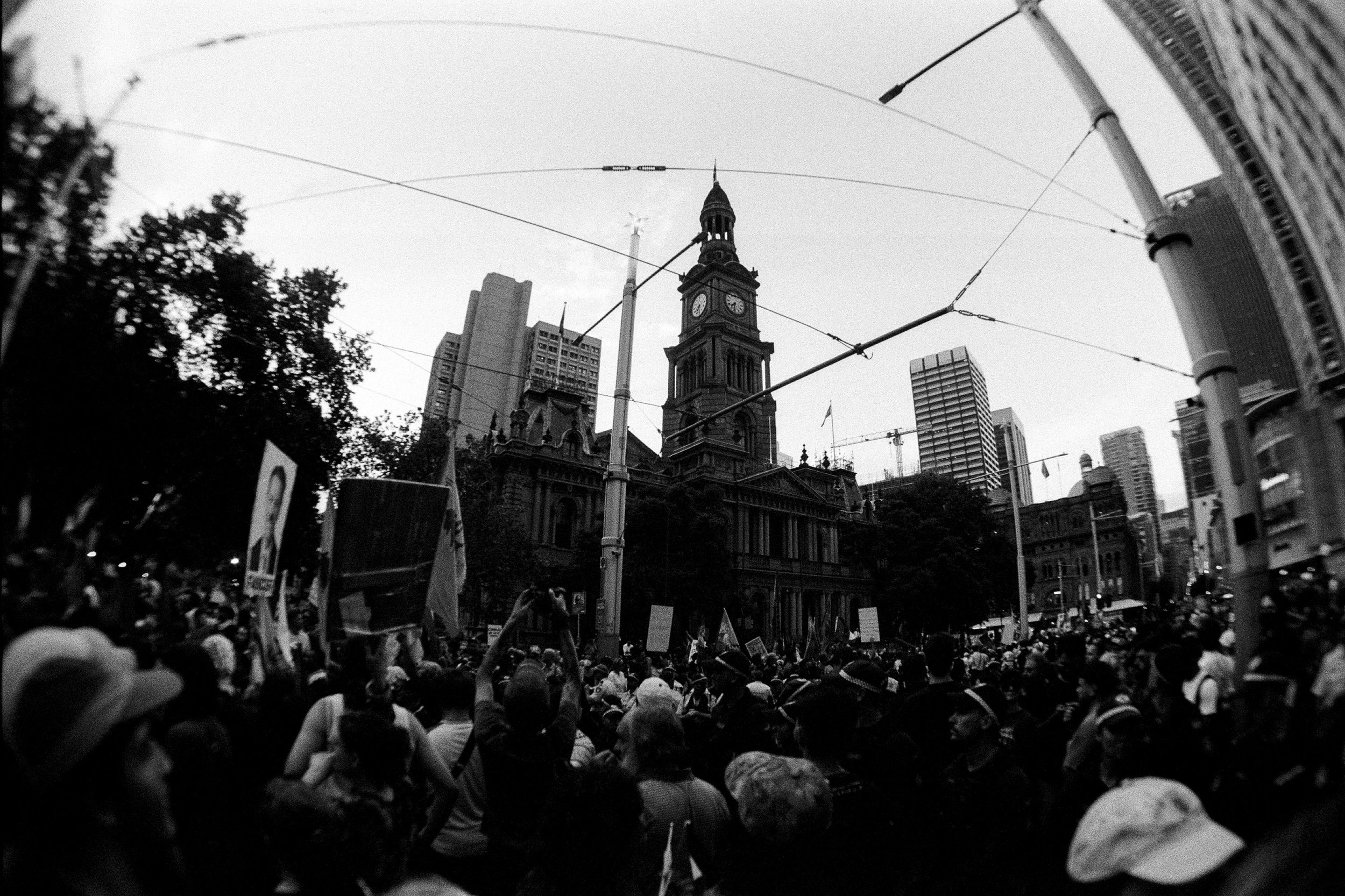 Large crowd gathered in Sydney CBD protesting the Australian visit of Israeli President Isaac Herzog, Palestinian flags visible — documentary photography by Elliott Deem.