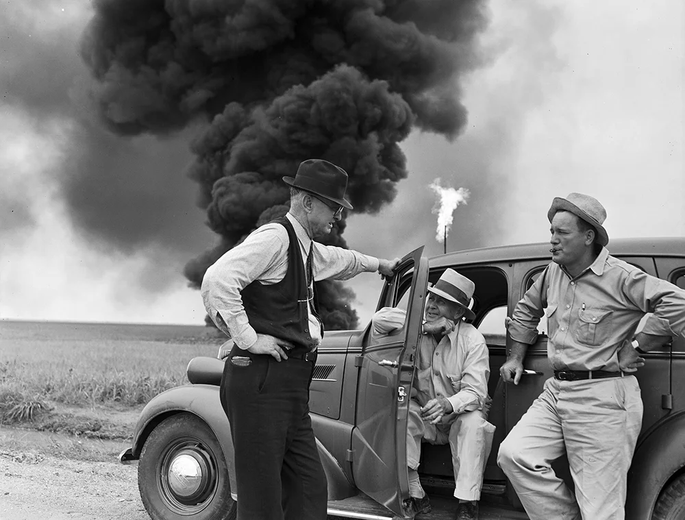 John_Butler_talks_with_two_men_while_oil_well_fire_burns_in_background_(9238328229).jpg