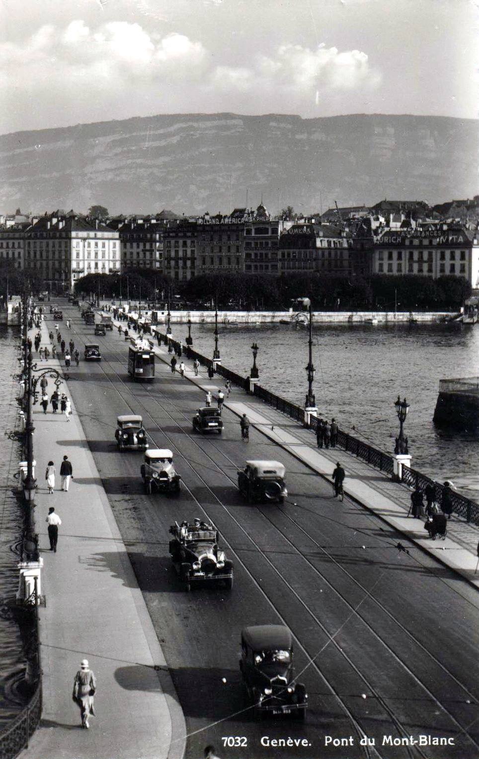 Vintage, black and white, postcard of Geneva with a view of the Mont Blanc bridge with a few cars and the Salève in the background.