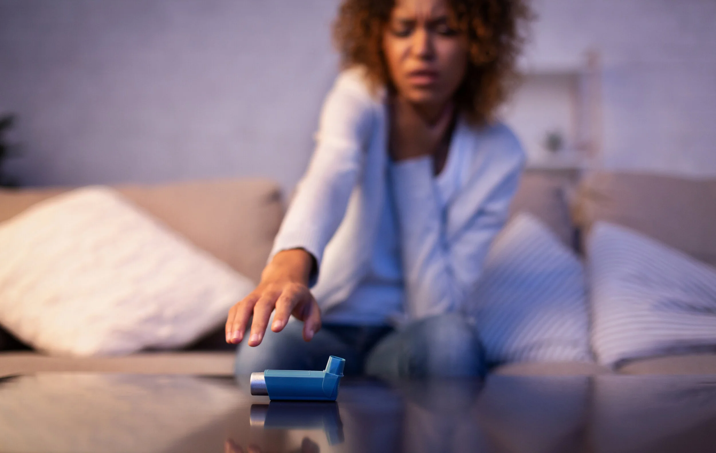 Copy of Asthma attack. Young woman reaching inhaler on table