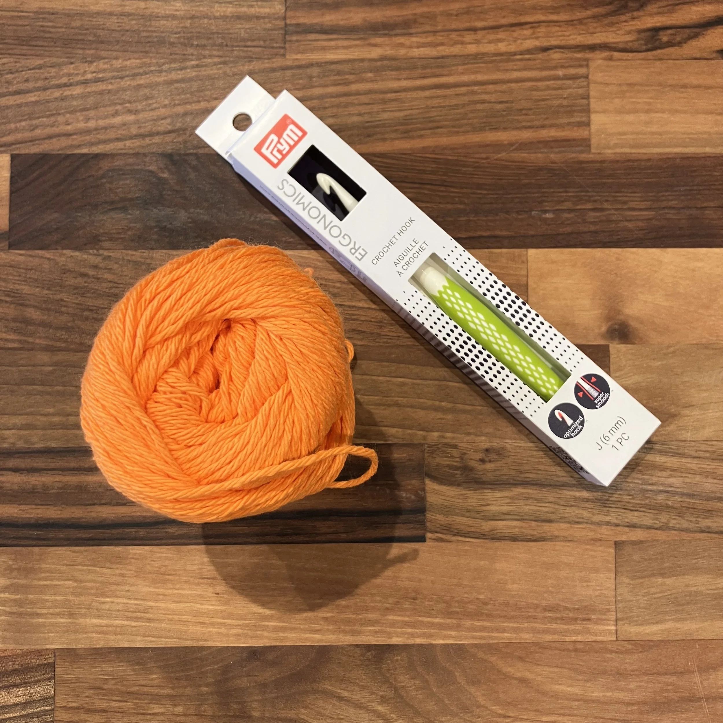 An orange ball of yarn next to a crochet hook on a wooden surface