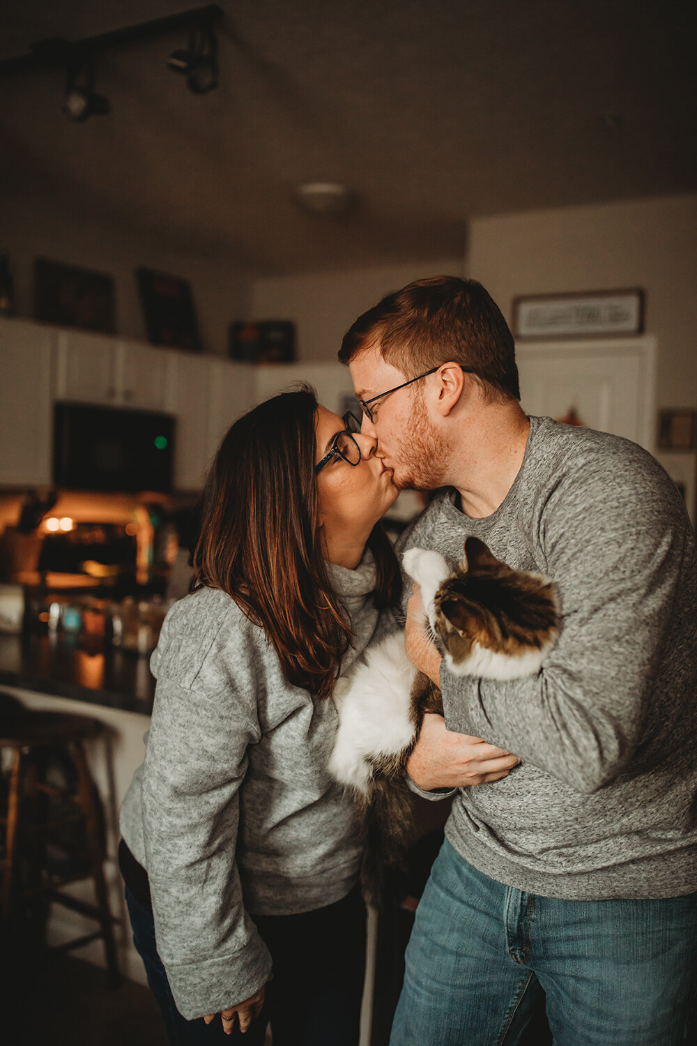 couple sharing a kiss while holding their cat 