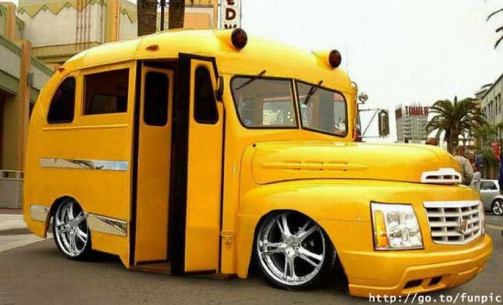 A creatively modified yellow bus with large chrome wheels and customized front grille.